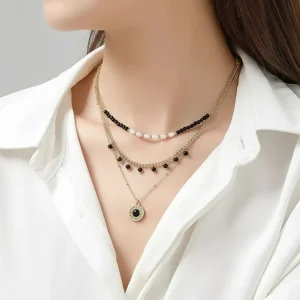 Γυναίκα φοράει το Belle Miss UMENO κολιέ με τριπλή αλυσίδα επιχρυσωμένου ατσαλιού, μαύρες πέρλες και φυσικές πέτρες.