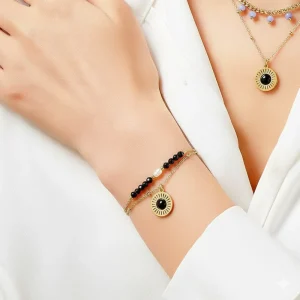 γυναίκα φοράει UMENO βραχιόλι διπλής αλυσίδας, επιχρυσωμένο ατσάλι, που αποτελείται από μία μαύρη πέρλα και χρωματισμένες φυσικές πέτρες. Layered βραχιόλι δώρο Κύπρος.